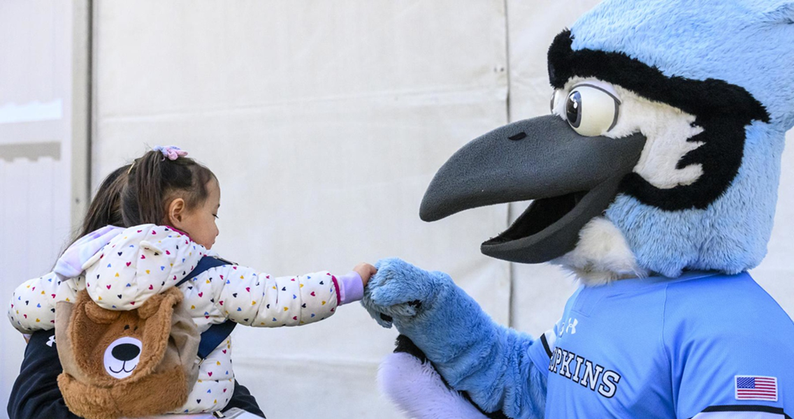 person in blue jay costume standing next to person holding child